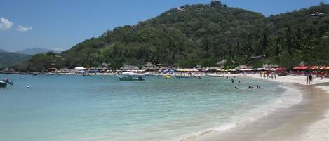 A beach with clear waters, boats, and umbrellas.