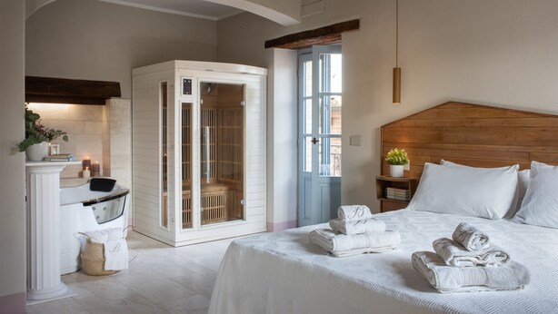 Ein Schlafzimmer mit einem großen Bett, einem Holz-Kopfteil, einem begehbaren Kleiderschrank und einem Badezimmer mit Badewanne und Waschtisch.