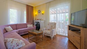 A living room with a sofa, armchair, and a television on a wooden cabinet. - Infinity Sunshine Villa (Mugla)