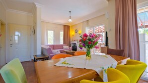 A dining area with a wooden table, yellow chairs, a vase with flowers, and a sofa in the background. - Infinity Sunshine Villa (Mugla)