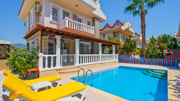 A swimming pool with lounge chairs, a covered patio, and a large house with a balcony. - Infinity Sunshine Villa (Mugla)