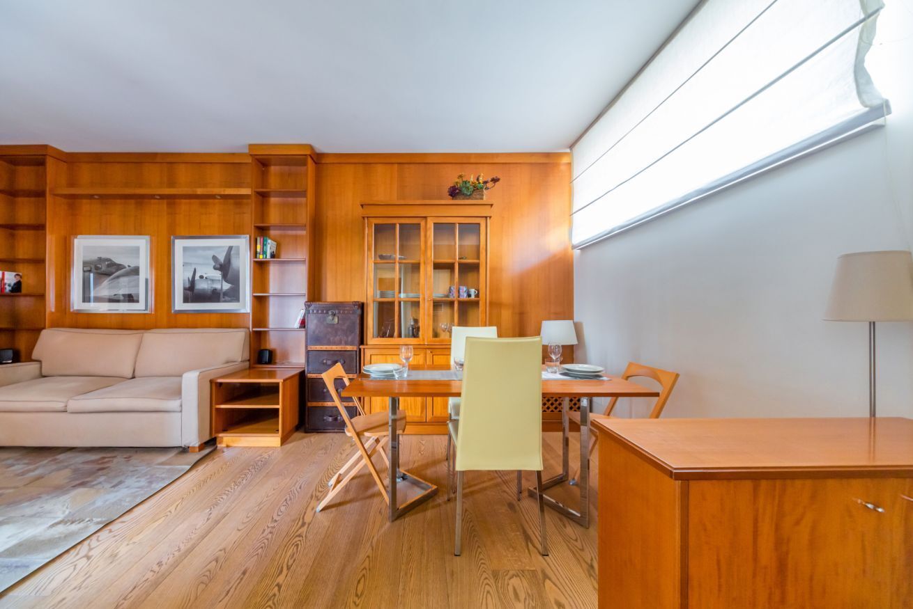 Um quarto com piso de madeira, um sofá, uma mesa de jantar com cadeiras, um armário e quadros nas paredes.