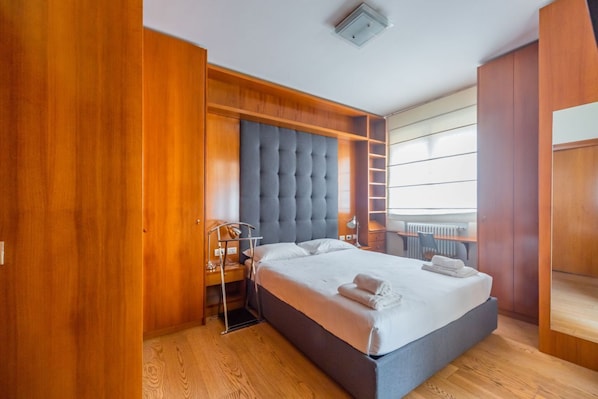 Une chambre à coucher avec un lit, une armoire en bois et une tête de lit rembourrée de couleur grise.