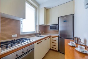 A compact kitchen with a gas stove, microwave, refrigerator, and a window providing natural light.