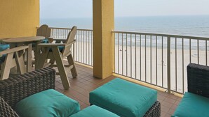 Een balkon met uitzicht op het strand, rieten meubels en een tafel met stoelen.