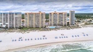 Een strandhotel met meerdere hoge gebouwen, een zandstrand met blauwe ligbedden en een zwembad.