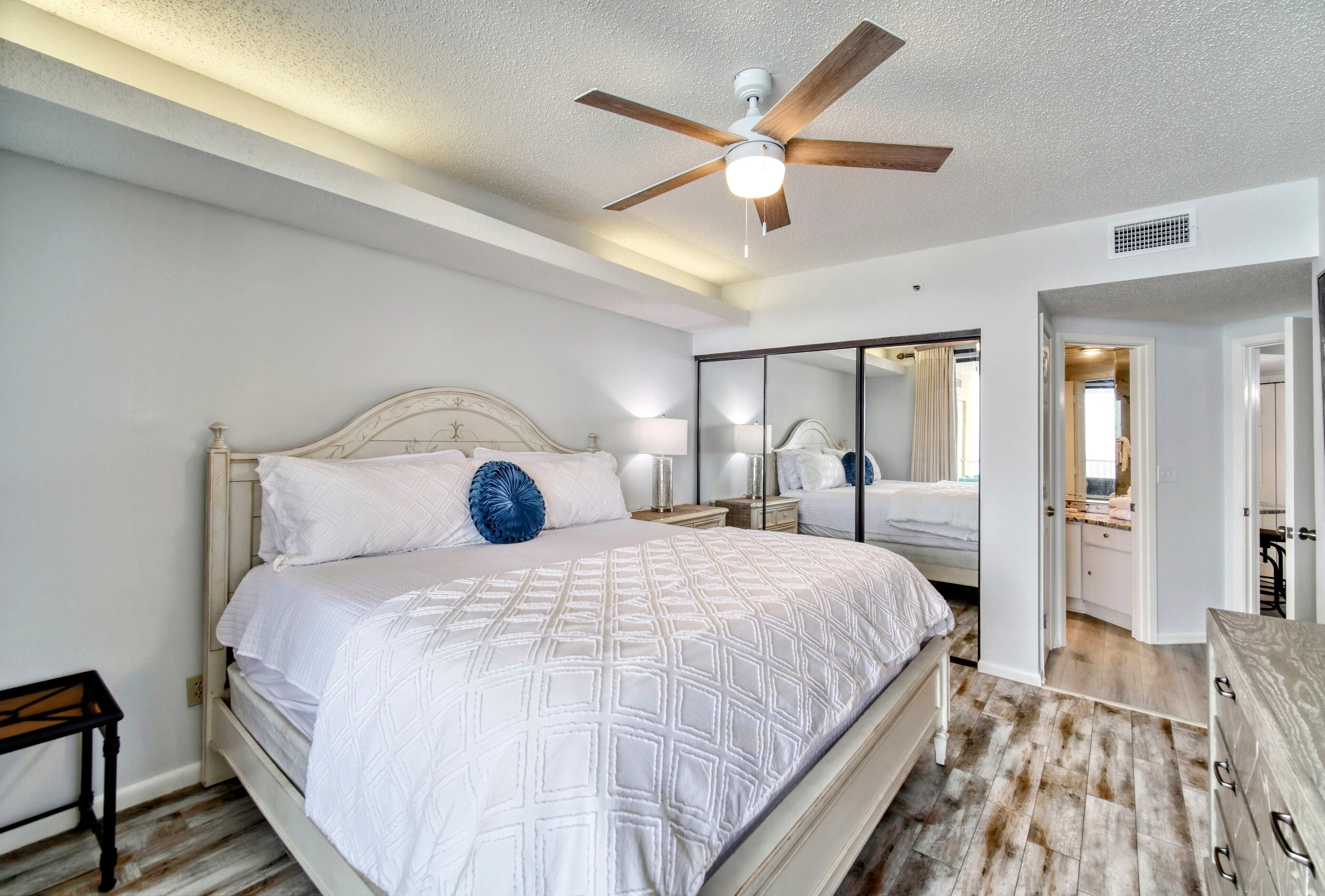 A bedroom with a bed, a ceiling fan, a nightstand, and a dresser.