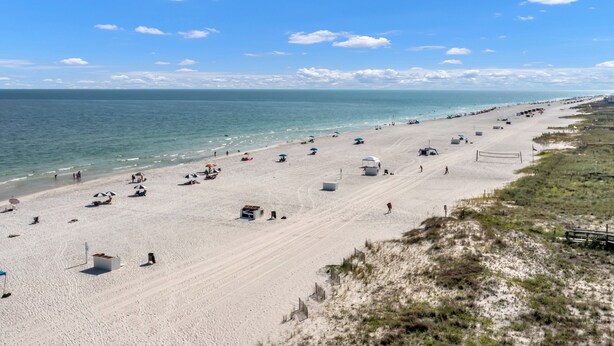 Een strand met een volleybalveld, parasols en mensen.