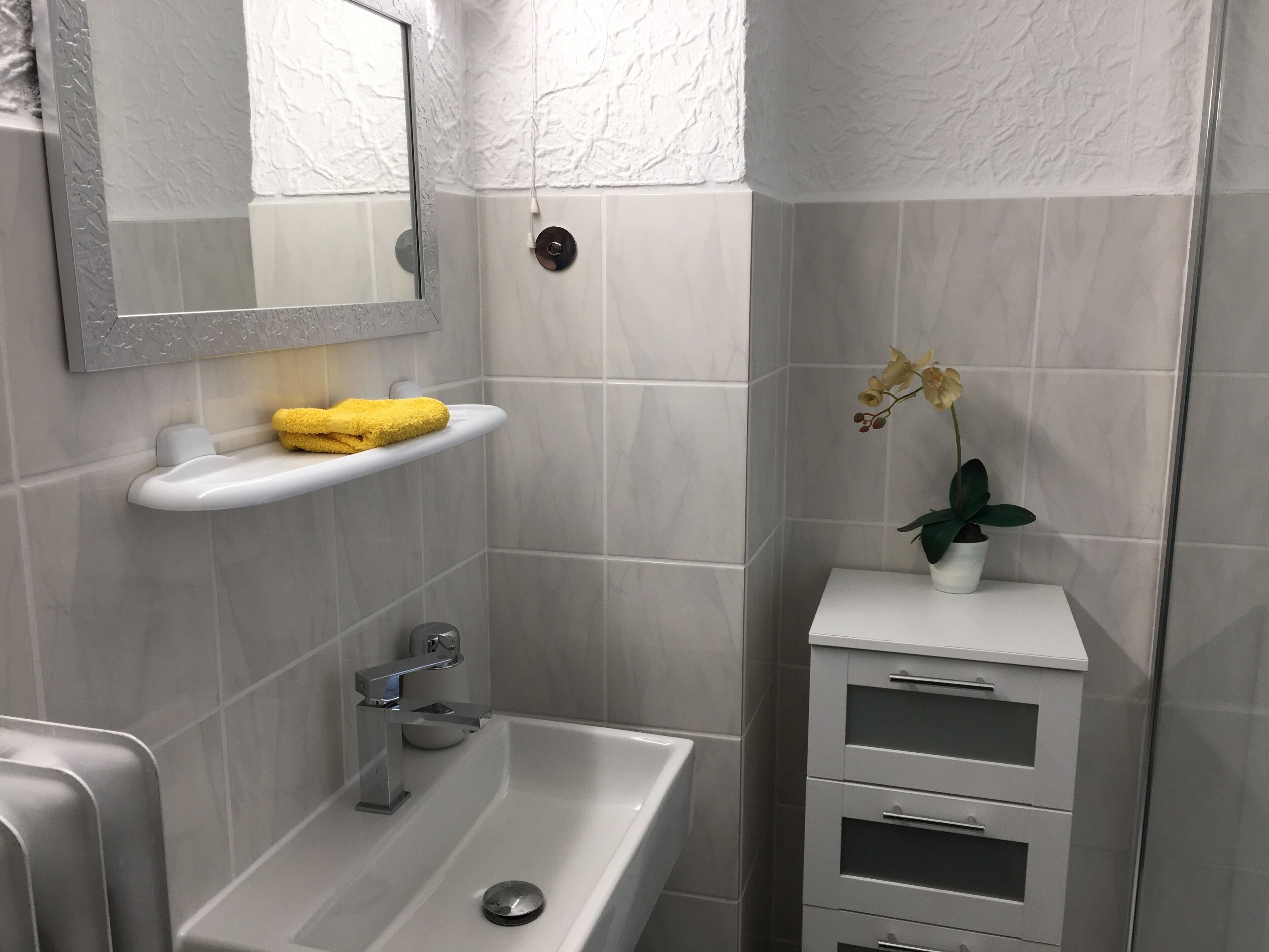 A bathroom with a white sink, a mirror, a yellow towel, and a potted orchid.
