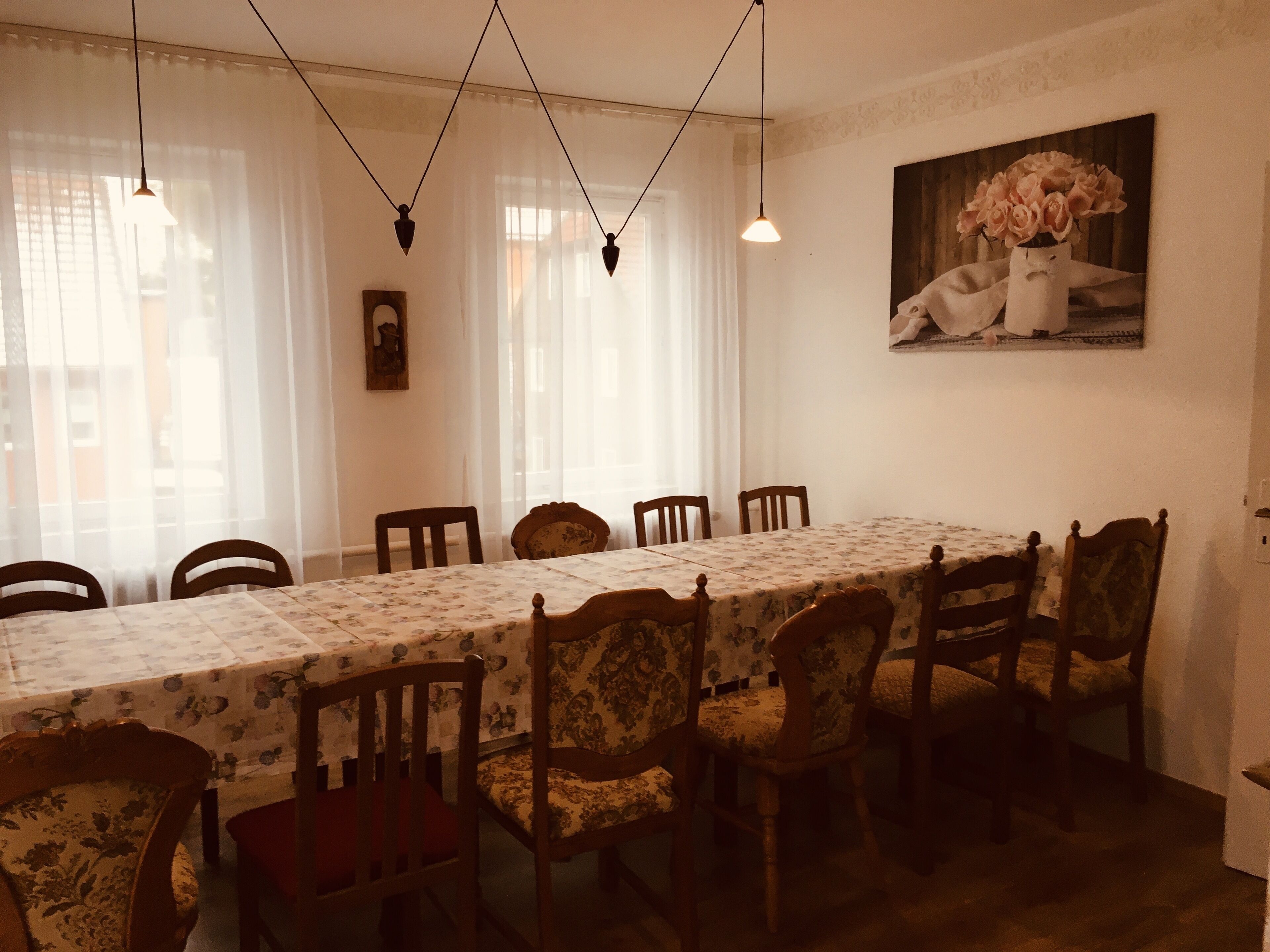 A dining room with a long table, chairs, and hanging lights.
