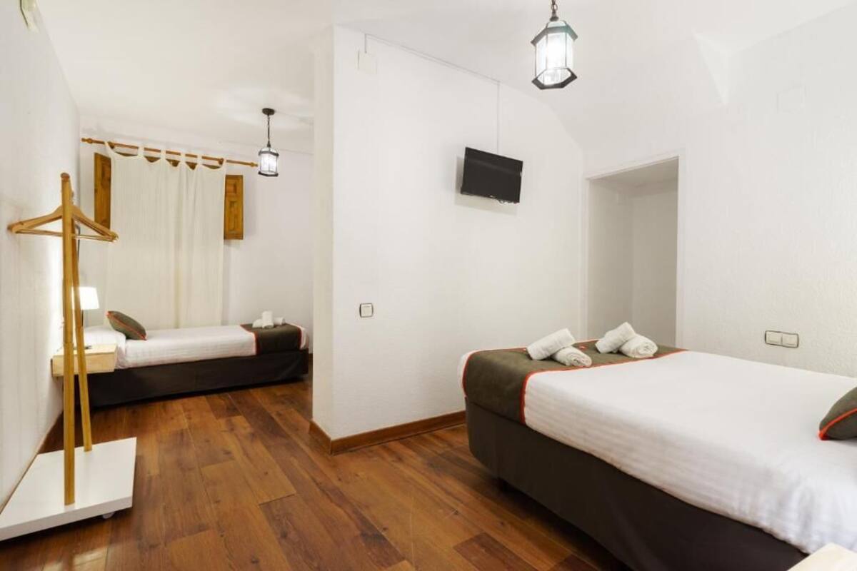 A hotel room with two beds, wooden flooring, a TV mounted on the wall, and a hanging light fixture.