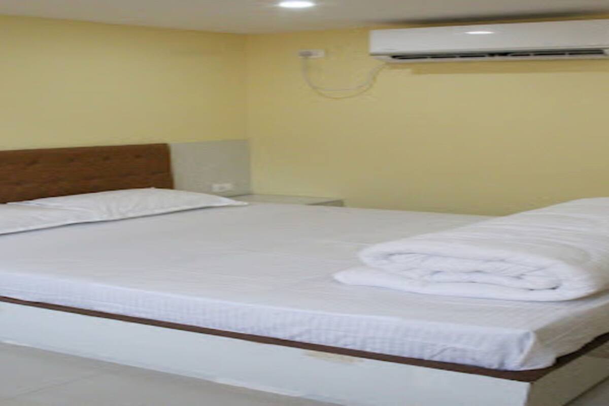 A hotel room with a bed, a nightstand, and an air conditioning unit on the wall.