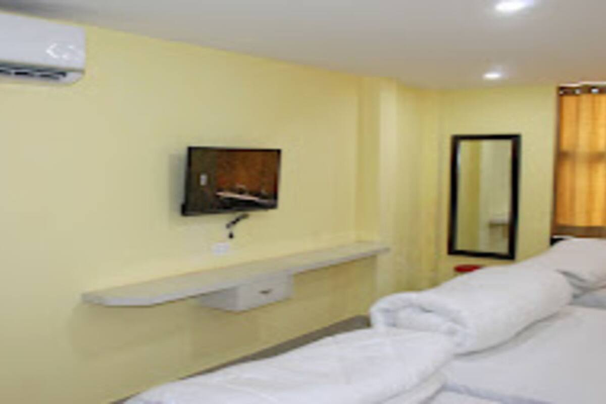 A hotel room with a bed, a bedside table, a mirror, and an air conditioning unit on the wall.