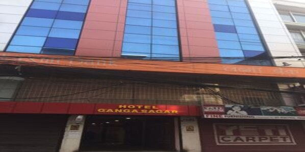 Un hotel con fachada roja y azul, un letrero visible que dice 'Hotel Gangasagar' y un anuncio de 'Fine Carpet' que indica servicio de alfombras.