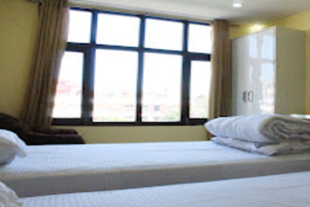 A hotel room with two beds, a window with curtains, a wardrobe, and a painting on the wall.