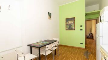A room with a dining table, chairs, a painting on the wall, and a white refrigerator.