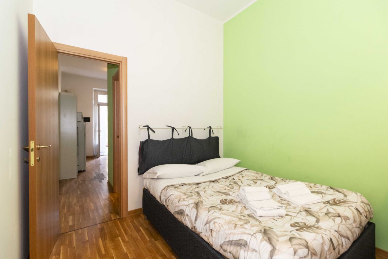 Ein Schlafzimmer mit einem Bett, einer Tür zu einem Flur und einer grünen Wand.