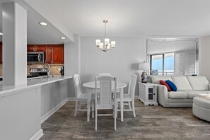 A modern kitchen with white cabinetry, a central island, and a dining area with white chairs.