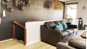A modern living room with a brown leather sofa, a wooden coffee table, and a brick wall adorned with various decorative masks. - Sea breeze Villa/walk everywhere/sunsets (Fremantle)