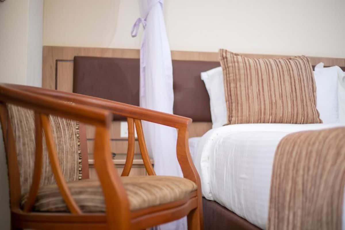A hotel room with a wooden chair, a bed with white and striped pillows, and a curtain.
