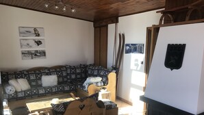 A cozy living room with a patterned sofa, wooden chairs, a fireplace, and wall art.