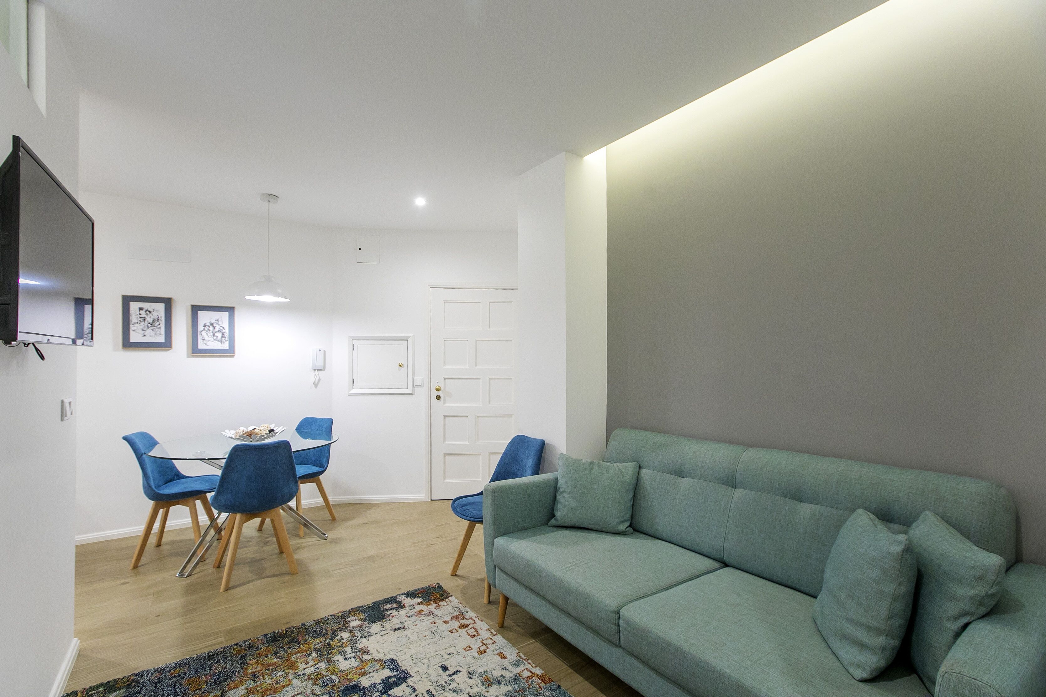 Una sala moderna con un sofá verde, sillas azules y una mesa de comedor de madera.