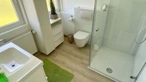 Un baño moderno con cabina de ducha de vidrio, un lavamanos blanco y un inodoro.