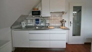 Una cocina compacta con armarios blancos, microondas, tetera y pileta.