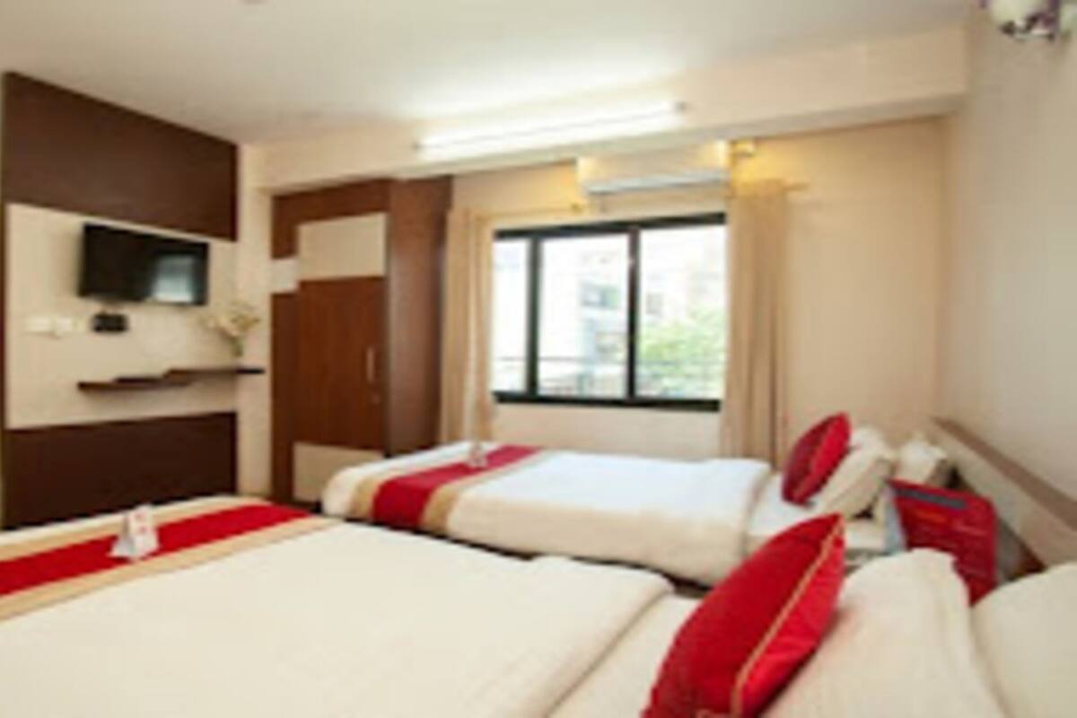 Habitación de hotel con dos camas, un televisor montado en la pared y una ventana con cortinas.