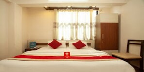 A hotel room with a bed, a nightstand, a chair, and a wardrobe. - MeroStay 022 Hotel Royal Kusum (Kathmandu)
