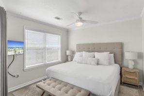 A bedroom with a bed, a ceiling fan, a window with blinds, and a nightstand with a lamp.
