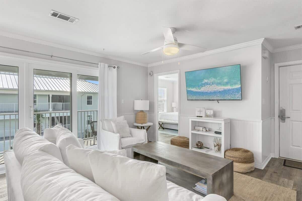 A modern living room with a white sofa, a coffee table, and a TV mounted on the wall.