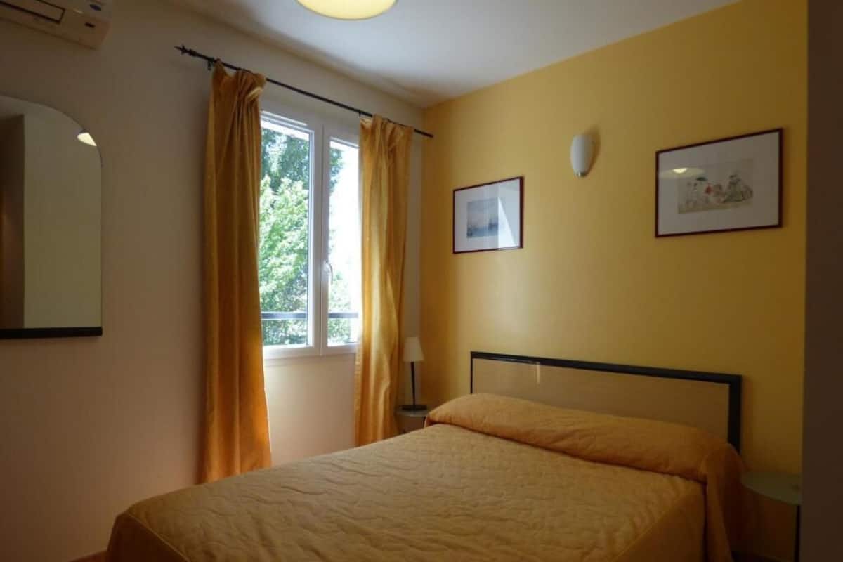 A bedroom with a bed, curtains, a window, and two framed pictures on the wall.