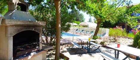 Eine Außenpatio mit einem Grill aus Stein, Picknicktischen und einem Pool im Hintergrund.