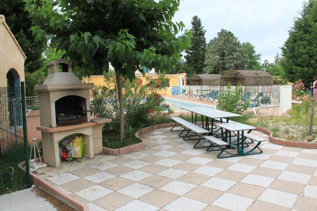 Un patio al aire libre con una parrilla, mesas de picnic y un área de piscina cercada.