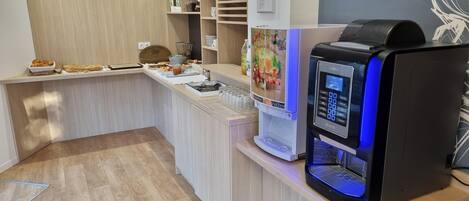 A breakfast bar with a coffee machine, a fruit juice dispenser, and a variety of pastries.