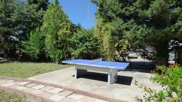 An outdoor ping pong table with a blue top and white sides, surrounded by a brick border and grass.