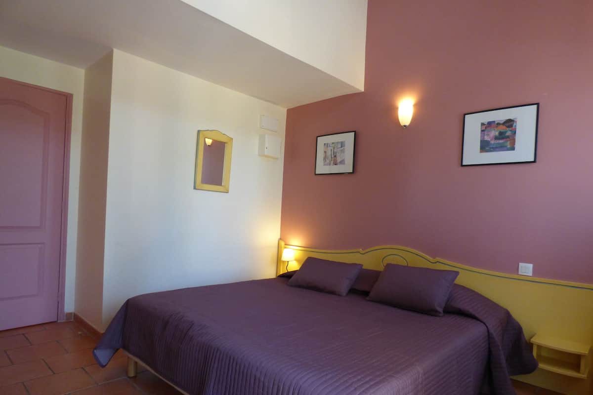 A bedroom with a bed, a door, a wall-mounted light, and a framed picture.