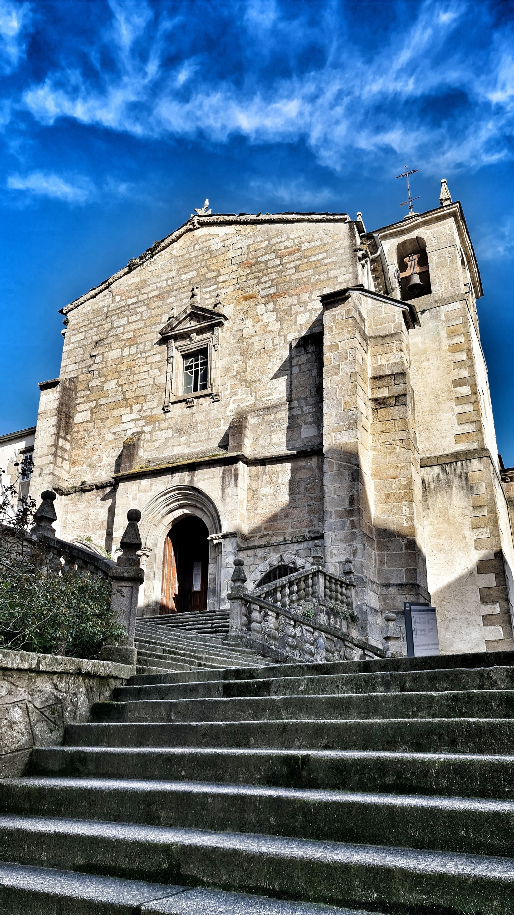A historic stone building with a bell tower, a large arched entrance, and a staircase leading up to the main entrance.