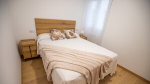A neatly made bed with a wooden headboard, a bedside table, and a nightstand. - Duerming Ría de Viveiro Apartamentos (Viveiro)