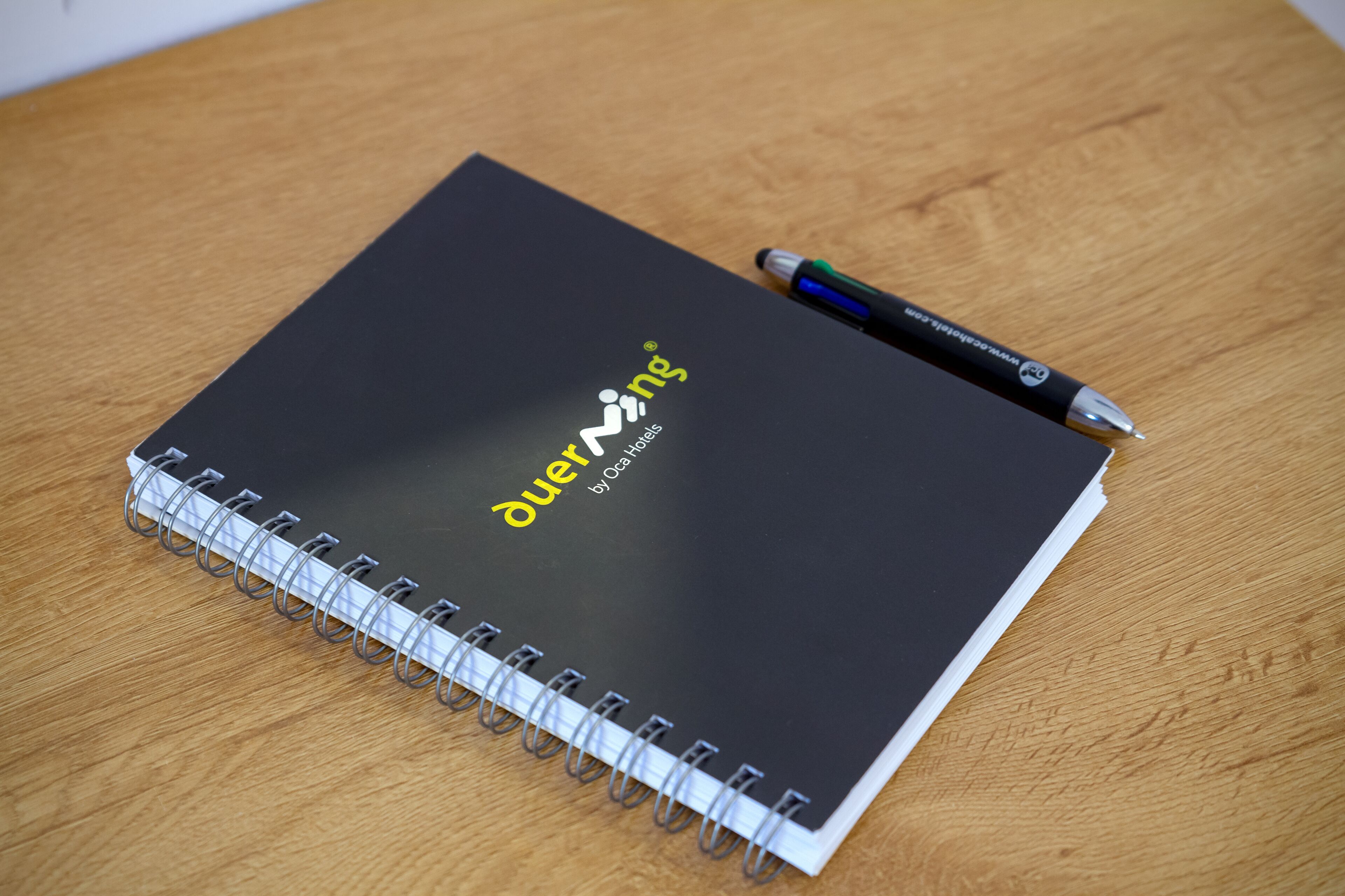 A spiral-bound notebook with a black cover and the text "duering" and "by Oca H. digital" on it.
