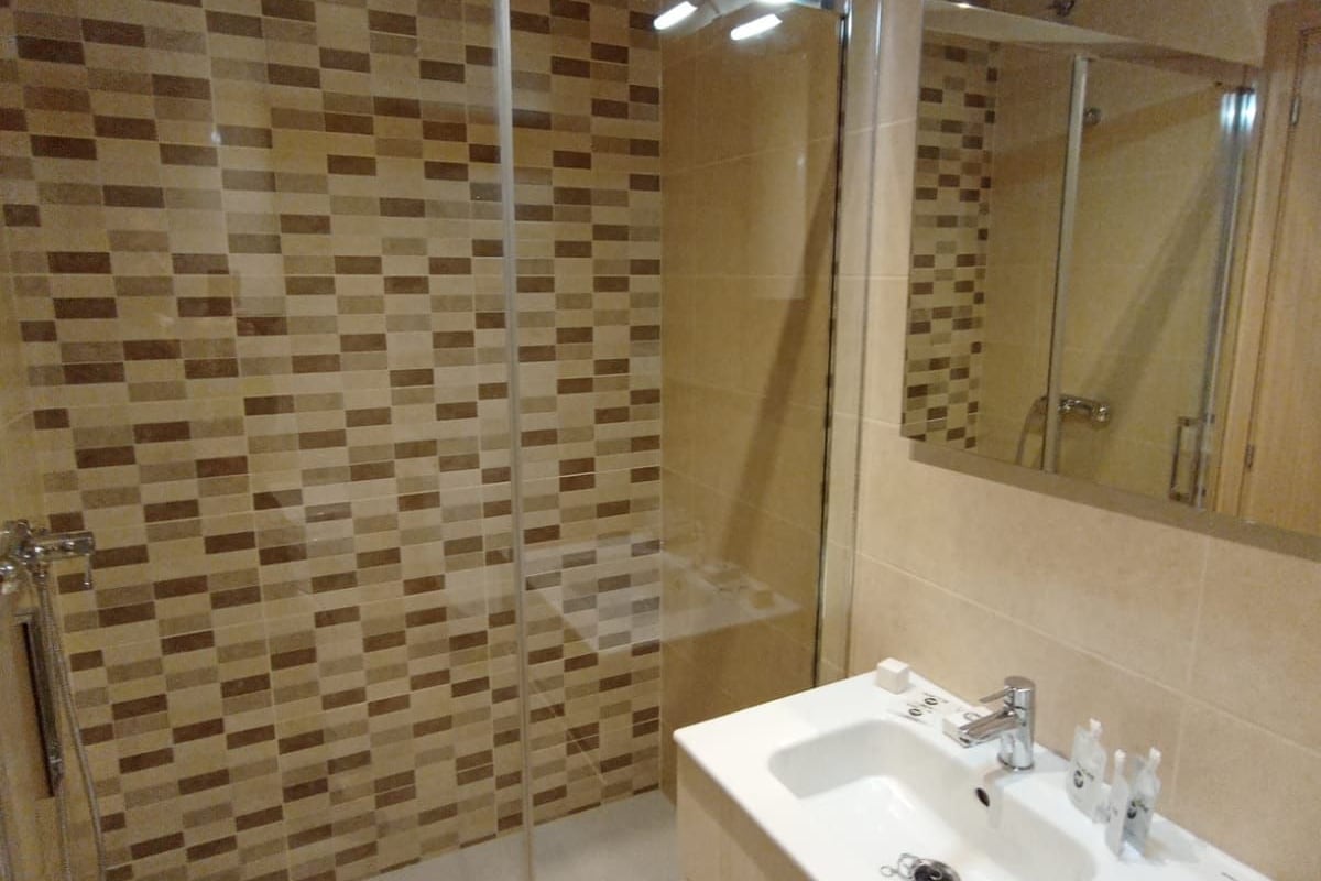 Un baño moderno con ducha de vidrio, lavamanos blanco y espejo grande.