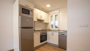 A modern kitchen with stainless steel appliances, white cabinetry, and a wooden floor. - Duerming Ría de Viveiro Apartamentos (Viveiro)