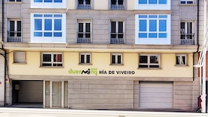 A multi-story building with a row of windows on each floor, a ground-level garage, and a sign for 'duerning RIA DE VIVEIRO'. - Duerming Ría de Viveiro Apartamentos (Viveiro)
