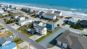 Uma área residencial costeira com casas ao longo da praia, vista clara do oceano e uma rua atravessando o bairro.