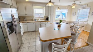 Uma cozinha moderna com armários brancos, uma geladeira de aço inoxidável, uma mesa de jantar com cadeiras e luminárias pendentes.