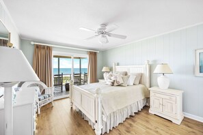 Une chambre à coucher comprenant un lit, des tables de chevet, un ventilateur de plafond, une vue sur l’océan et un balcon aménagé avec du mobilier d’extérieur.