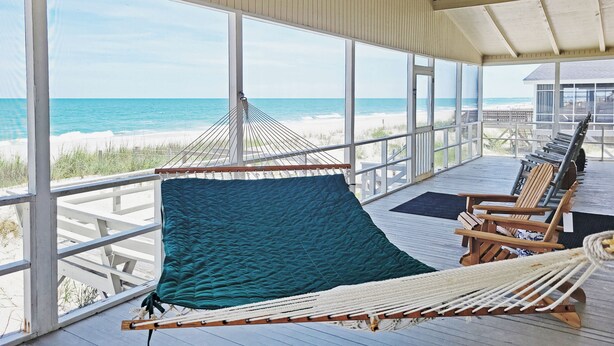 Een kamer aan het strand met een hangmat, houten stoelen en uitzicht op de oceaan.