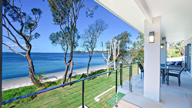 Un balcon avec vue sur la mer, une pelouse et un espace détente avec une table et des chaises.