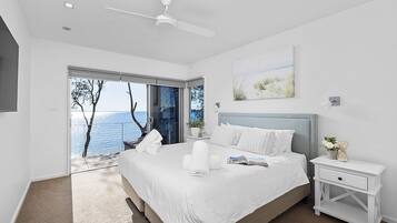 Ein modernes Schlafzimmer mit einem großen Bett, einem Nachttisch, einem Deckenventilator und Meerblick durch eine Schiebetür.